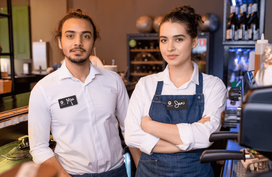 Man and Woman coworkers at a cafe wearing white shirts and name tags that read 'Mick' and 'Jen'